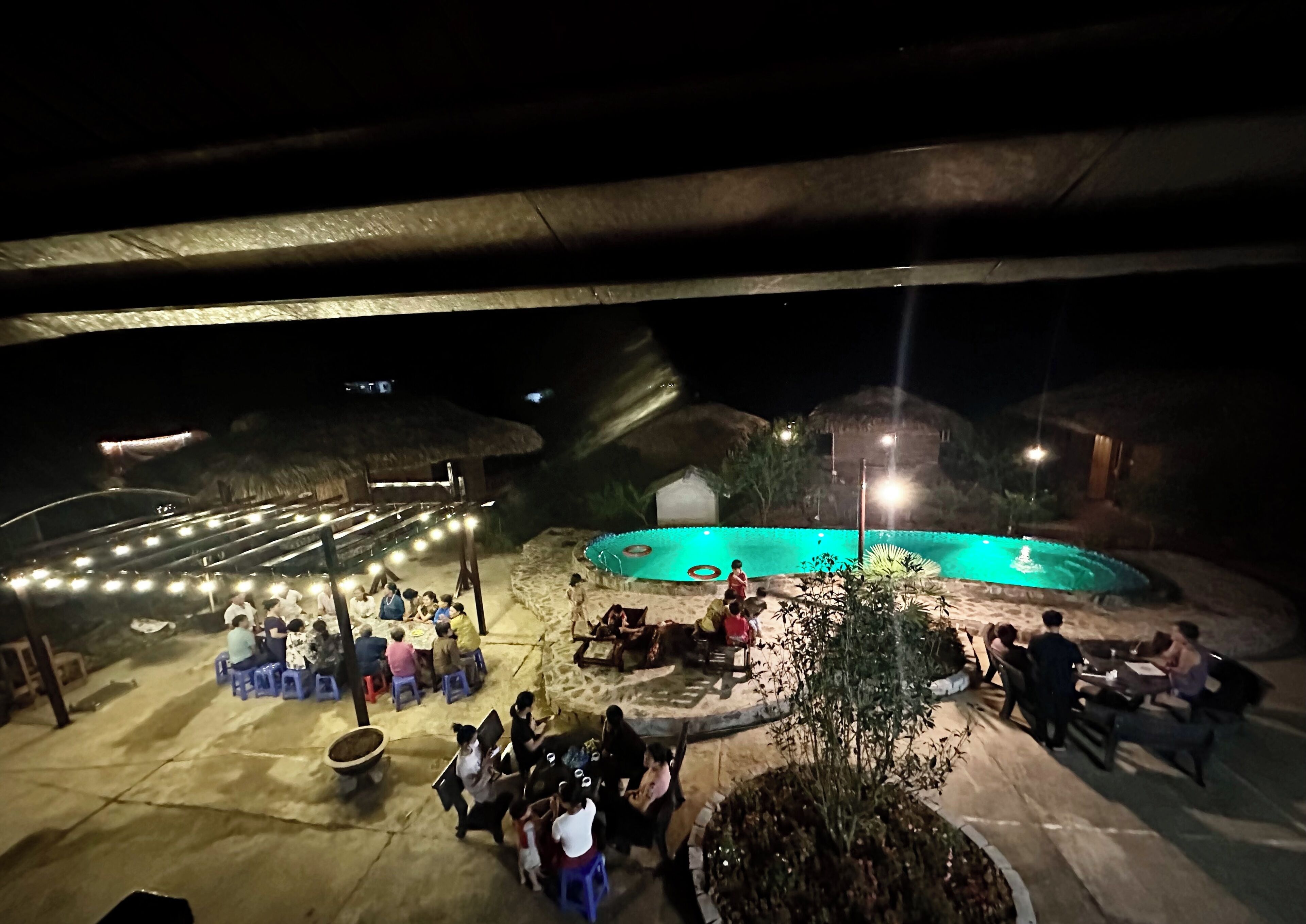 An outdoor area with a swimming pool, seating arrangements, and a covered section with string lights.