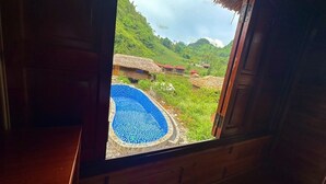 A view from a window of a room with a pool, surrounded by lush greenery and thatched-roof buildings. - Bac Ha Lodge Reatreat (Bac Ha)