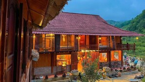 A wooden house with a red-tiled roof, multiple balconies, and a well-lit interior. - Bac Ha Lodge Reatreat (Bac Ha)