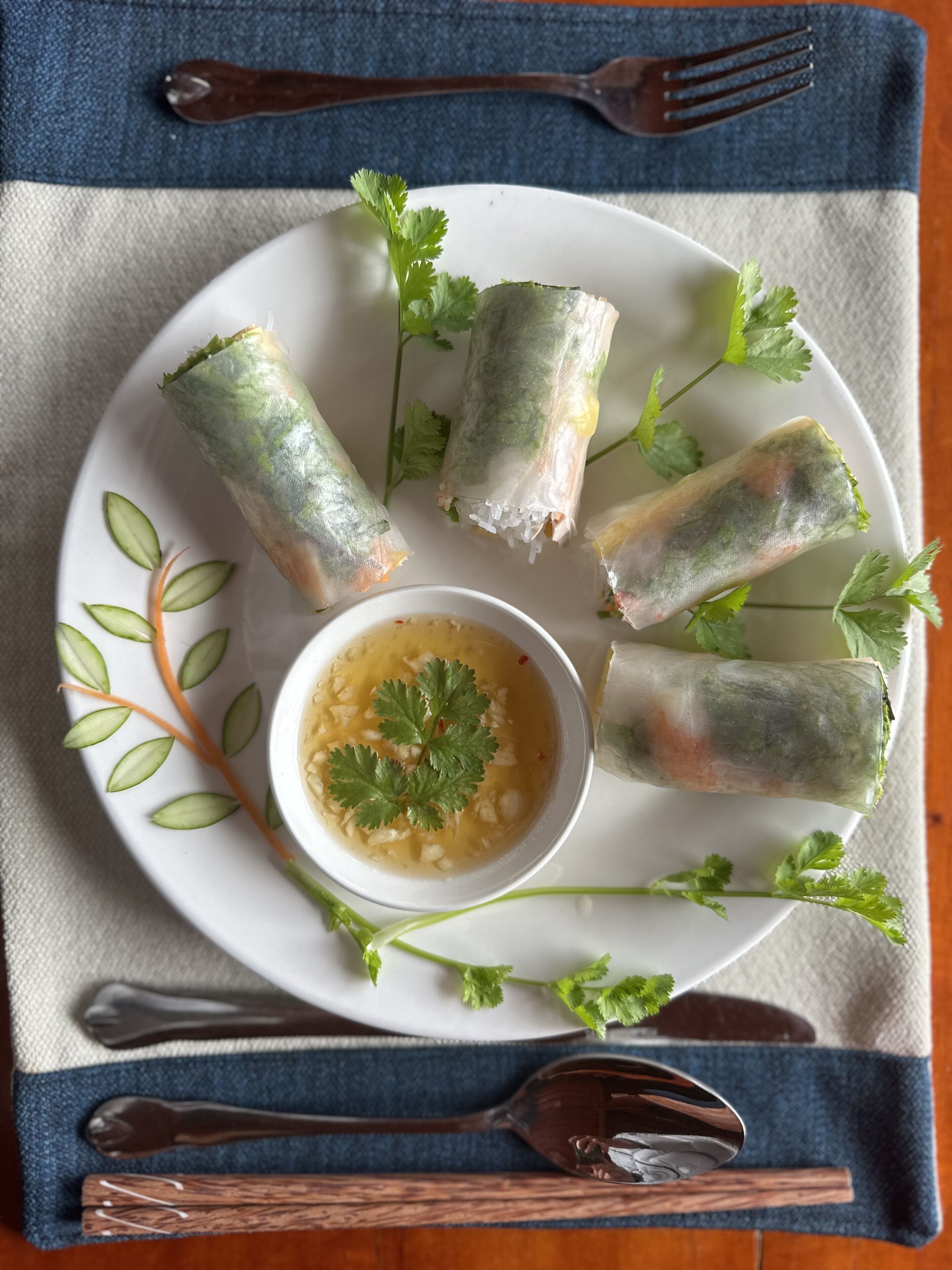 A plate of spring rolls with a dipping sauce, garnished with cilantro, on a white plate.