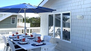Et udendørs spiseområde med et bord dækket til fire personer, en parasol og et hvidt hegn i baggrunden.