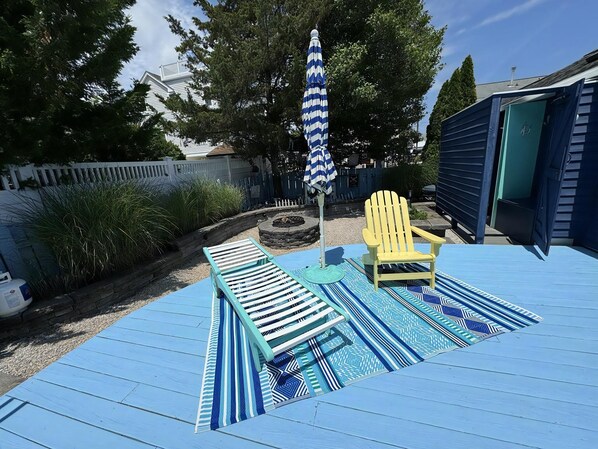 A deck with lounge chairs, a patterned rug, and a striped umbrella.