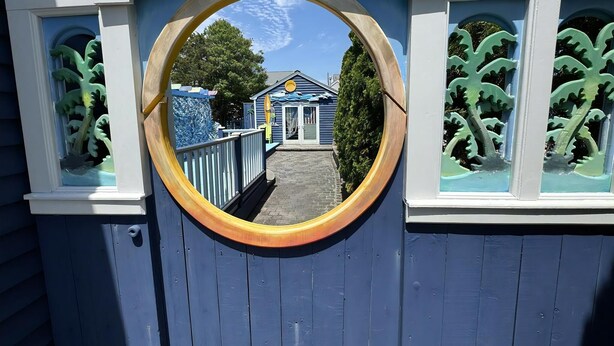 Una ventana circular que muestra un edificio con tejado azul y adornos blancos.
