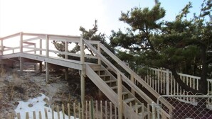Eine hölzerne Treppe führt zu einem überdachten Bereich, umgeben von einem Zaun und Bäumen.