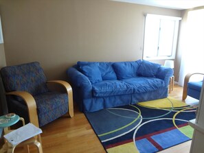 Una sala de estar con un sofá azul, un sillón estampado y una mesita de noche con una lámpara.
