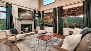 A cozy living room with a fireplace, wooden walls, and large windows. - Relax'd Retreat Couples Cabin with Hot Tub-Fire Pit-View-Deck (Sevierville)