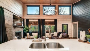 A spacious kitchen with a large island, double sinks, and a built-in stove. There are multiple windows providing natural light and views of the outdoors. - Relax'd Retreat Couples Cabin with Hot Tub-Fire Pit-View-Deck (Sevierville)