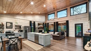 A spacious kitchen with a central island, wooden floors, and large windows offering views of the outdoors. - Relax'd Retreat Couples Cabin with Hot Tub-Fire Pit-View-Deck (Sevierville)