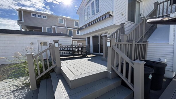 A residential deck with a wooden railing, a trash bin, and a clear sky.