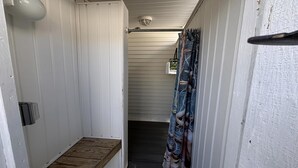 A narrow hallway with a wooden bench, white walls, and a patterned curtain.