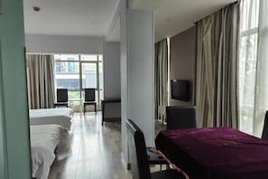 A hotel room with a bed, a desk with a purple tablecloth, a TV on the wall, and a view of the outside through large windows. - Xin'anjiang Hotel (Jiande)