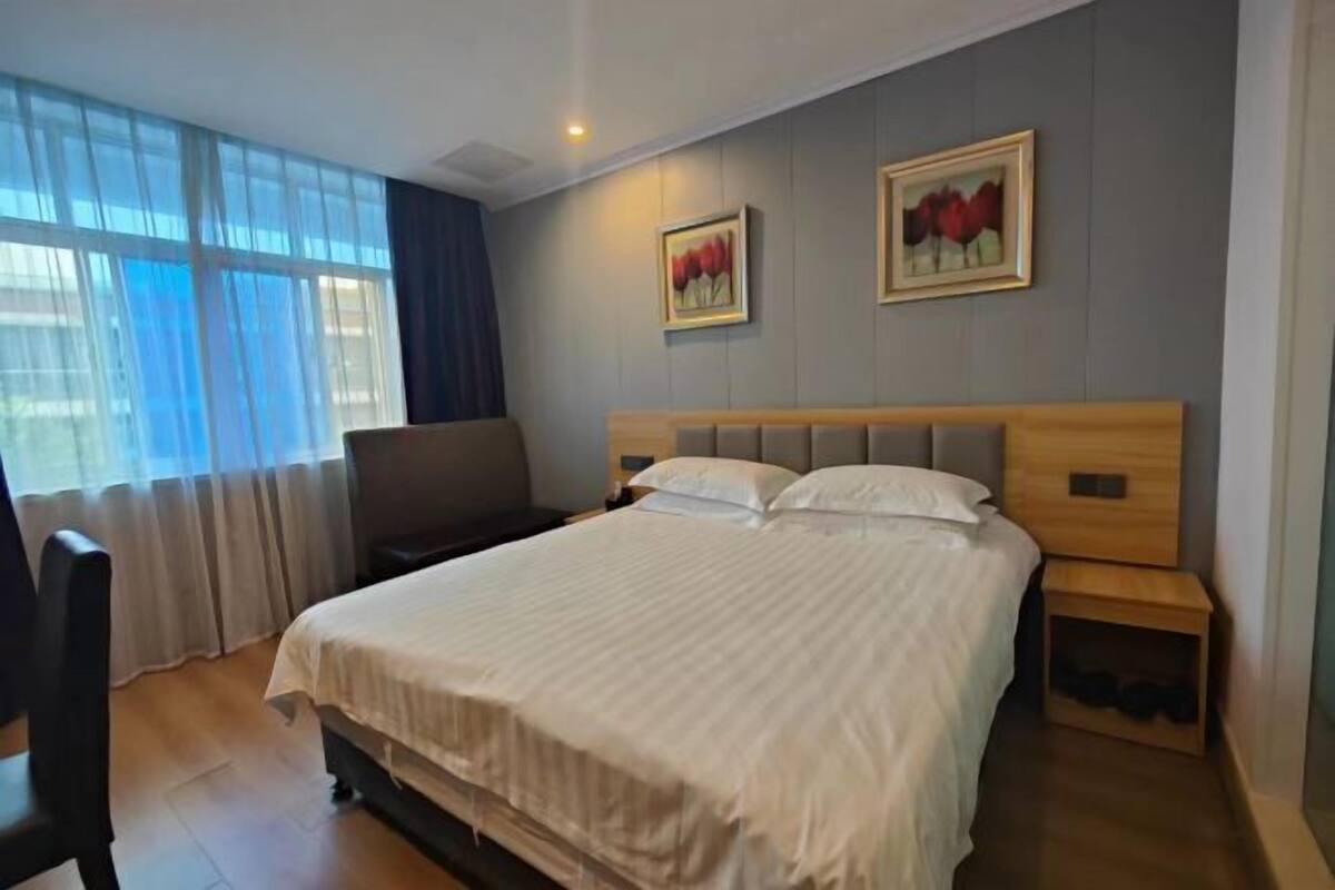 A hotel room with a large bed, a bedside table, a chair, and a window with curtains.