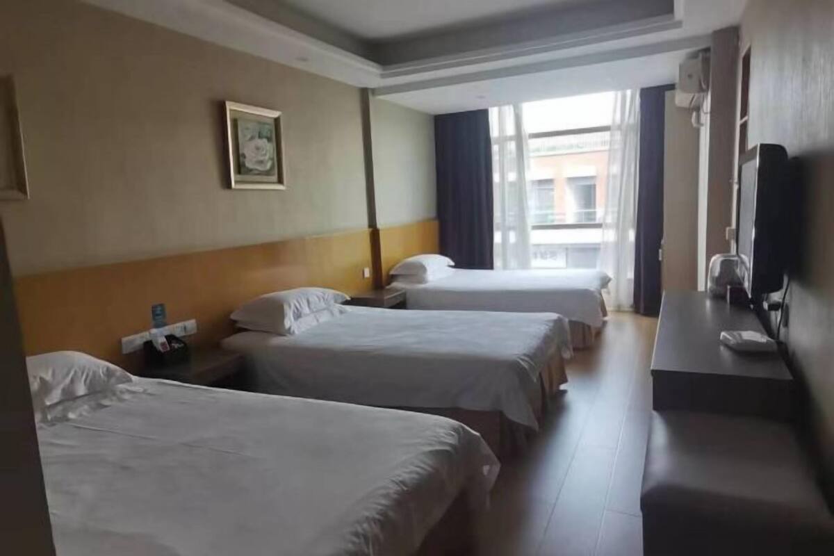 A hotel room with three single beds, a desk with a chair, a television, and a window with curtains.