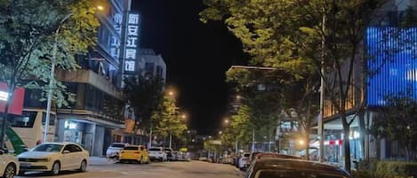 A nighttime street scene with parked cars and illuminated buildings.