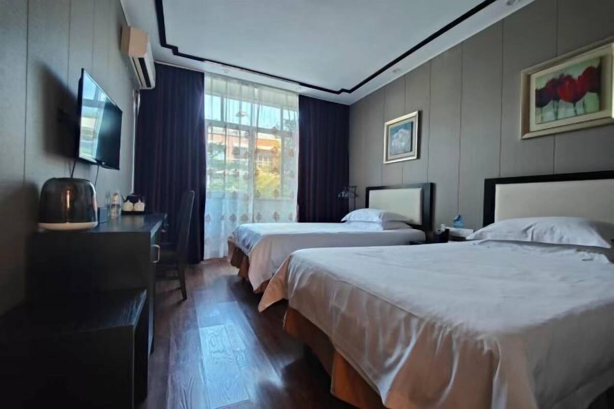 A hotel room with two beds, a TV, a desk, and a window with curtains.