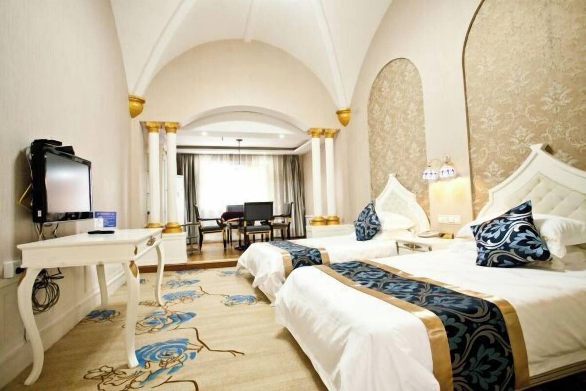 A hotel room with two beds, a desk, a television, and a view of the hallway.