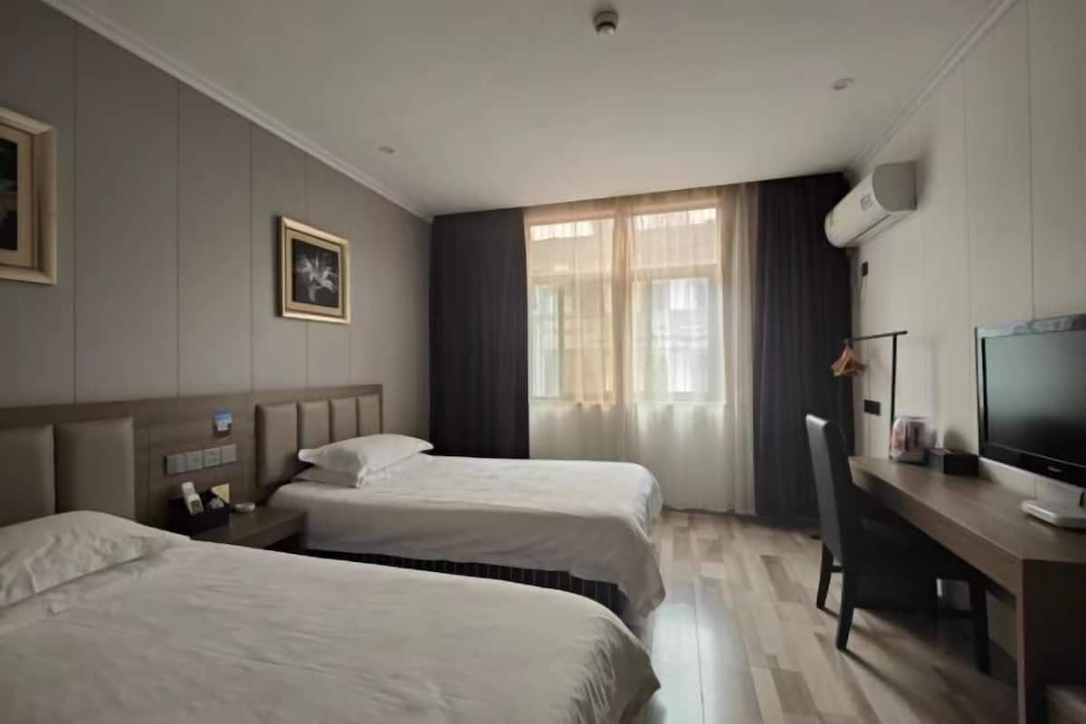 A hotel room with two beds, a desk with a computer, and a large window with curtains.