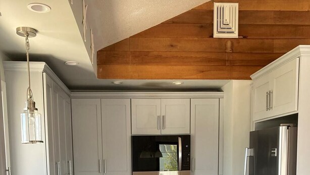 Eine moderne Küche mit weißen Schränken, Edelstahlgeräten, einer Holzbalkendecke und einer gefliesten Spritzschutzwand.