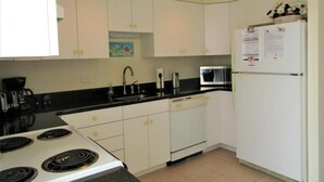 Una cocina con armarios blancos, estufa, microondas, refrigerador y pileta.