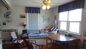 Una habitación acogedora con una cama, una mesa de comedor y sillas. Cuenta con un ventilador de techo, una ventana con cortinas y decoración en las paredes.