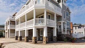 A multi-story residential building with a balcony on the second floor, stone foundation, and a clear sky. - VIEWS AND A POOL! PERFECT VACATION HOME! (Brant Beach)