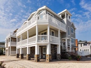 A multi-story residential building with a balcony on the second floor, stone foundation, and a clear sky.