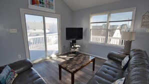 A living room with a large sectional sofa, a coffee table, a flat-screen TV, and a view of a balcony with a railing.