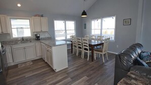 A spacious kitchen with a dining area, wooden flooring, and large windows.