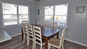 A dining area with a wooden table and chairs, large windows with blinds, and a hanging light fixture.