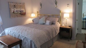 A bedroom with a large bed, two bedside tables with lamps, a bench, and a wall-mounted picture.