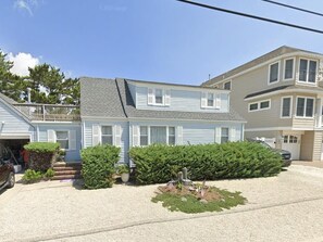 Uma casa residencial de dois andares com varanda frontal, um pequeno jardim com peça decorativa e garagem.