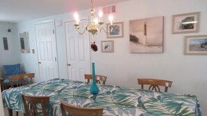 A dining room with a table covered in a tropical leaf tablecloth, surrounded by wooden chairs.