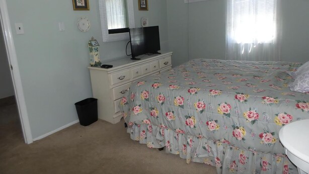 Une chambre à coucher comprenant un lit, une commode, un téléviseur et une fenêtre avec des stores.
