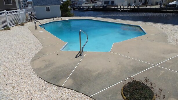 Una piscina con plataforma de hormigón, rodeada por una valla blanca y una masa de agua.
