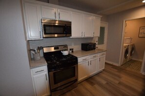 Kitchen area with microwave, oven, stove, kettle, and coffee maker, along with a laundry area and wooden flooring.
