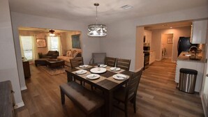 Un comedor con una mesa de madera dispuesta para seis personas, un sofá y una cocina al fondo.