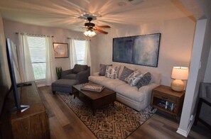 A living room with a sofa, coffee table, and a TV. There is a ceiling fan, a lamp, and a bookshelf. - Beautiful 4 Bedroom in quiet neighborhood! (Bedford)
