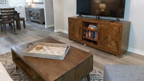 Una sala de estar con una mesa de centro de madera, un televisor sobre un mueble de madera y una estantería.