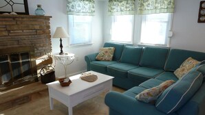 A living room with a sofa, a coffee table, a lamp, a fireplace, and windows with curtains. - Oceanside 3 Bedroom, 1 Bath Duplex - A Short Walk to the Beach! (Beach Haven Crest)
