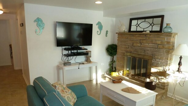 A living room with teal sofas, a flat-screen TV, a fireplace, and decorative wall art. - Oceanside 3 Bedroom, 1 Bath Duplex - A Short Walk to the Beach! (Beach Haven Crest)