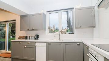 Een moderne keuken met grijze kastjes, een vaatwasser, een spoelbak en een raam met decoratieve objecten.