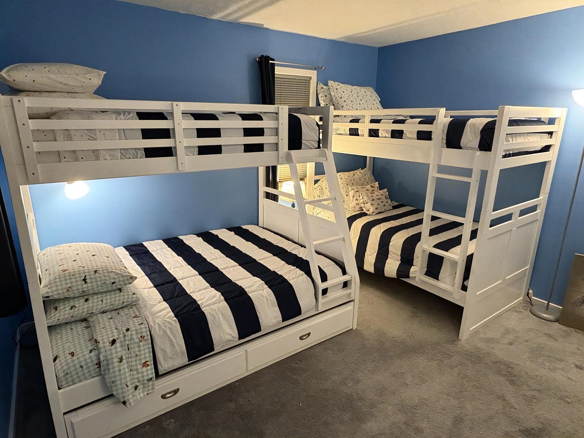 A bunk bed room with blue walls, a window with blinds, and a lamp.