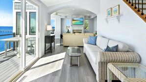 En rummelig opholdsstue med balkon, sofa, sofabord og et køkken i baggrunden.