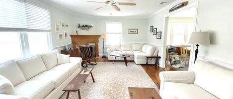 A living room with a white sofa, a wooden coffee table, a fireplace, and a ceiling fan.