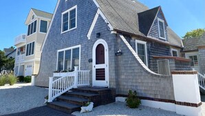 A two-story house with a grey shingle exterior, a white front door, and a small porch with steps. - LBI vacation rental property (Brant Beach)