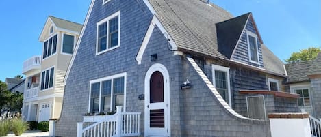 A two-story house with a grey shingle exterior, a white front door, and a small porch with steps.