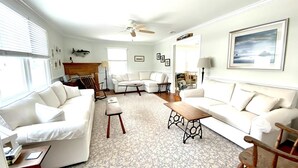 A living room with a ceiling fan, white sofas, a patterned rug, and a wooden coffee table. - LBI vacation rental property (Brant Beach)
