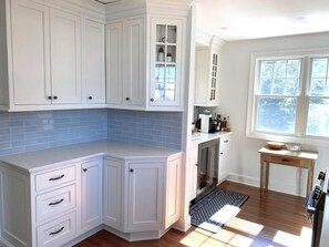 A kitchen with white cabinetry, a blue-tiled backsplash, a stainless steel refrigerator, and a window with a view of trees. - LBI vacation rental property (Brant Beach)