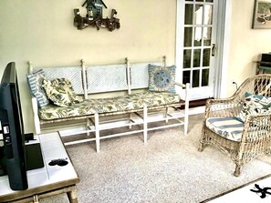 A room with a white sofa, a wicker chair, a television on a table, and a door with glass panels. - LBI vacation rental property (Brant Beach)