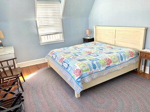 A bedroom with a bed, a nightstand, a lamp, a chair, and a window with blinds. - LBI vacation rental property (Brant Beach)